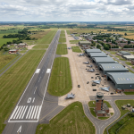 Current image: Military airbase runway with fighter jets parked by hangars and a control tower